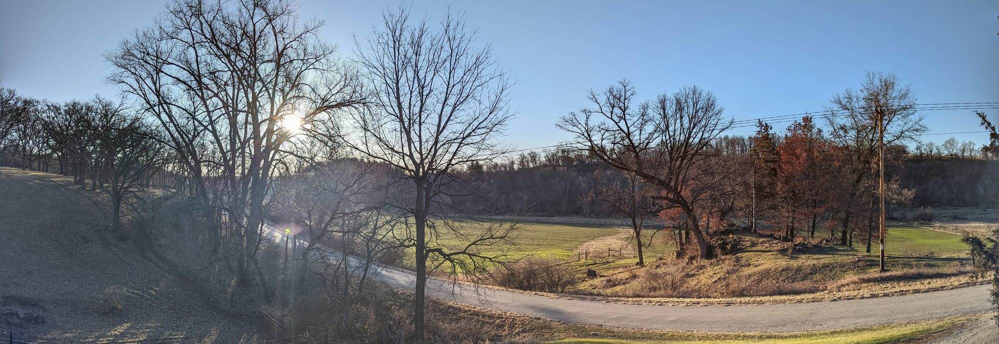 Bare oaks and low December sun over a Driftless coulee, an empty two-lane road curving along the valley floor.